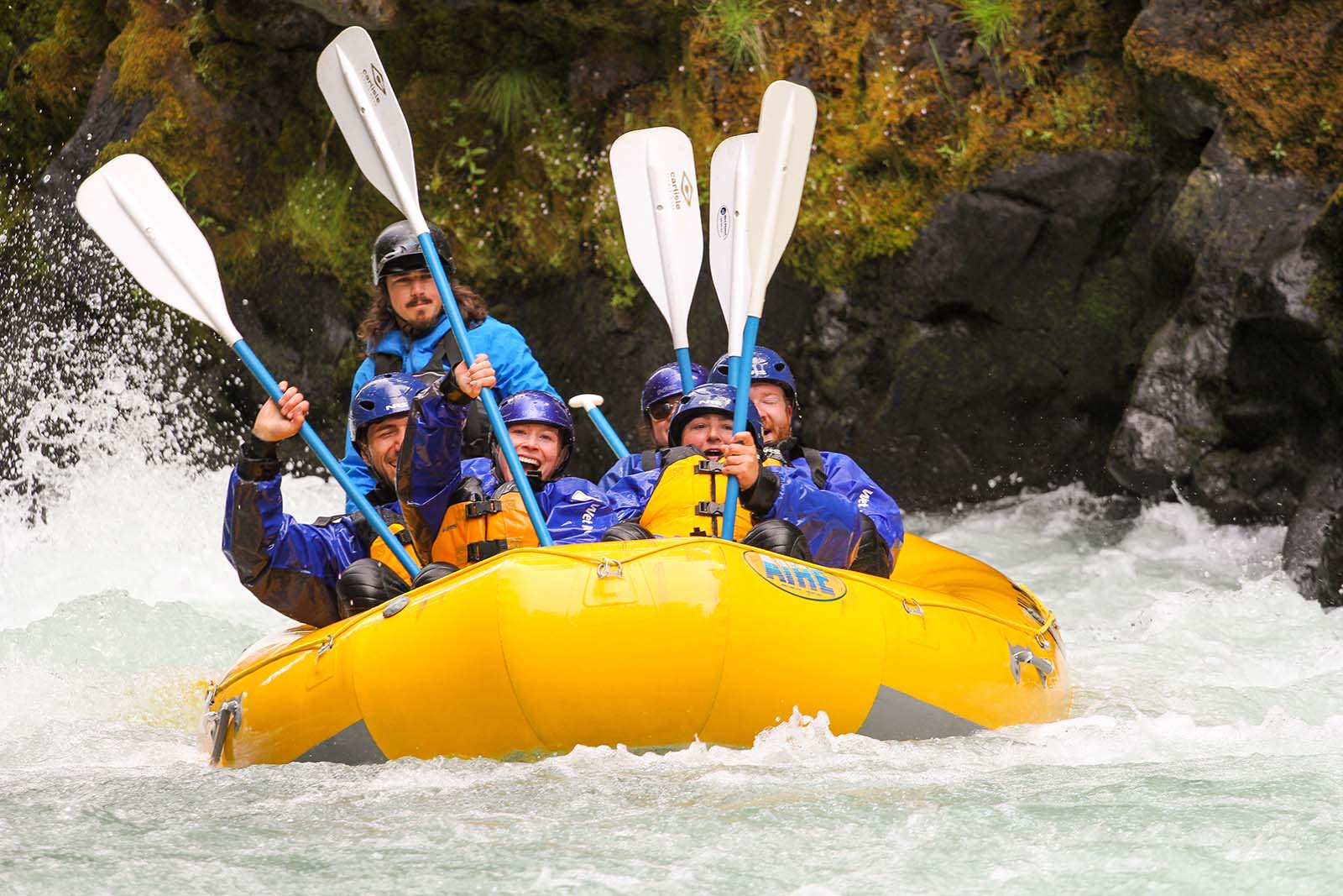 wet-planet-happy-rafters river rafters with paddles up in yellow raft